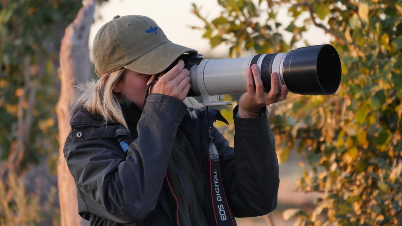 Frau mit Kappe h&auml;lt Kamera mit Zoom Objektiv