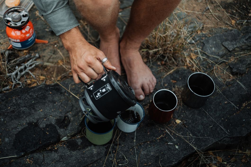 Vier Metalbecher werden mit einem warmen Getränk auf dem Kalahari Primitive Trail von einem Teilnehmer gefüllt