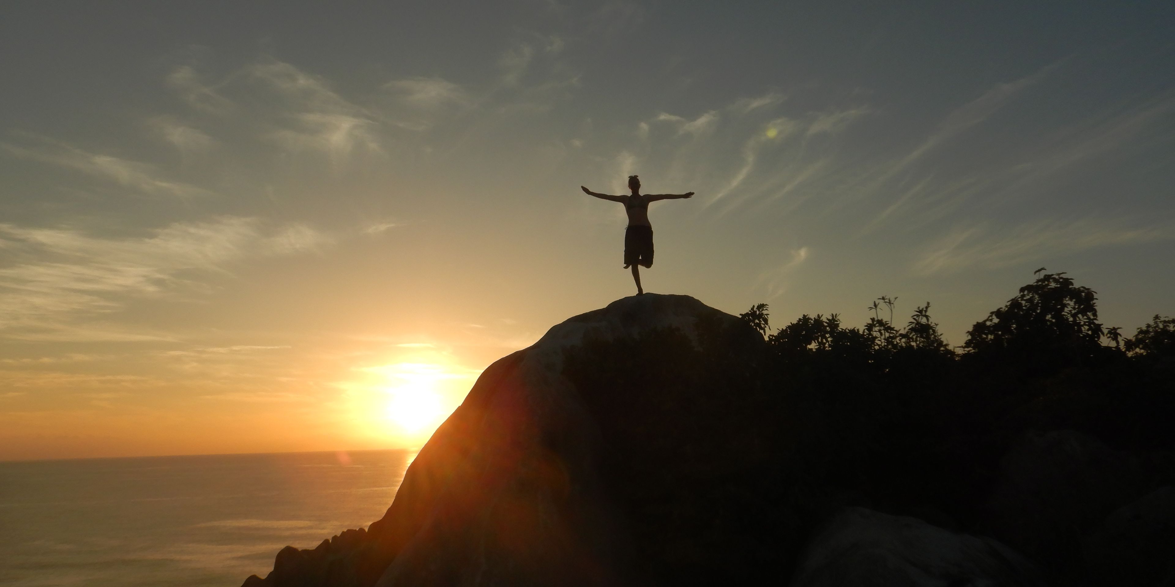 A volunteer in our species conservation project in the Seychelles is standing on a rock at sunset