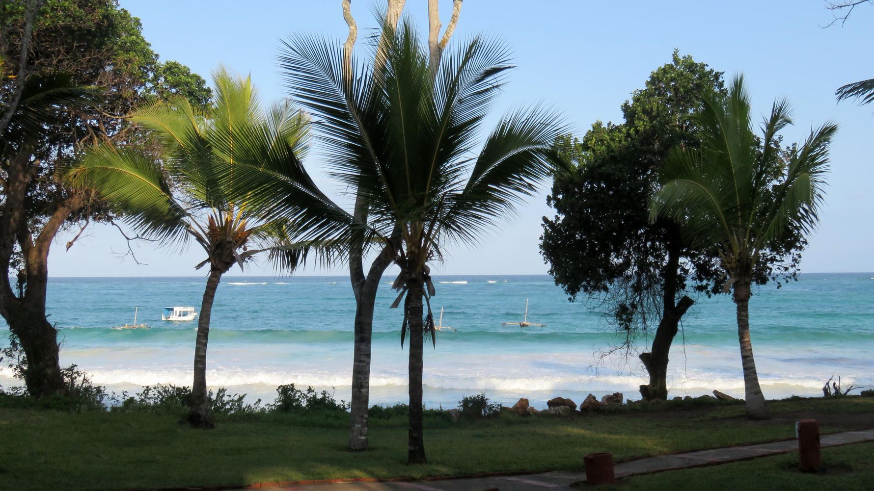 Afrika-Urlaub Ostafrika: Strandszene mit Palmen, Meer und Booten in Kenia am Indischen Ozean