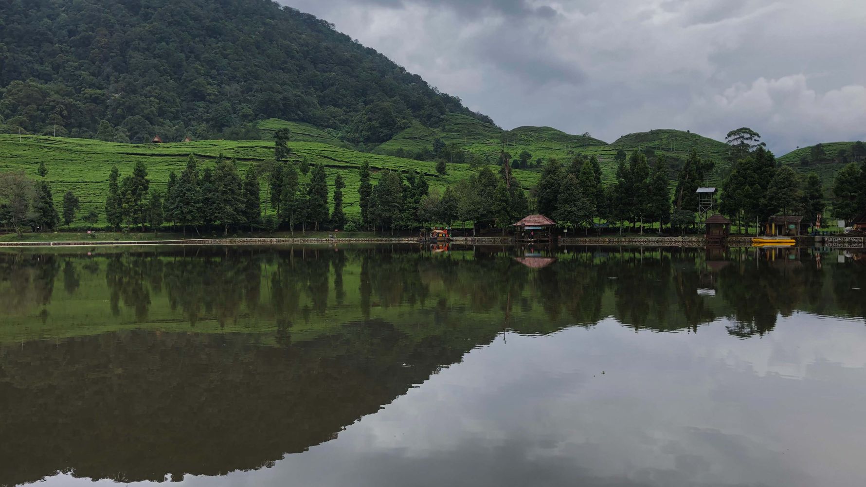 Ein ruhiges Gewässer mit begrüntem Ufer in Indonesien, Südost Asien. Im Hintergrund erstreckt sich ein Berg, der bewaldet ist.