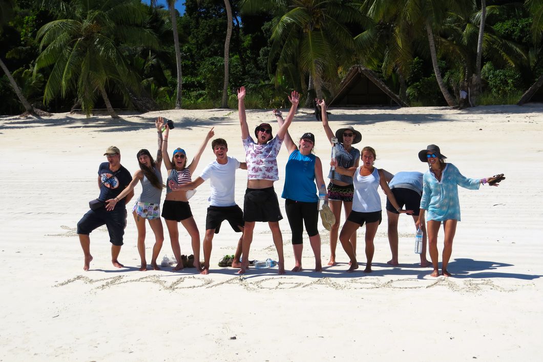 Freiwillige Helfer werfen am Strand von Madagaskar ihre Arme in die Hoehe.