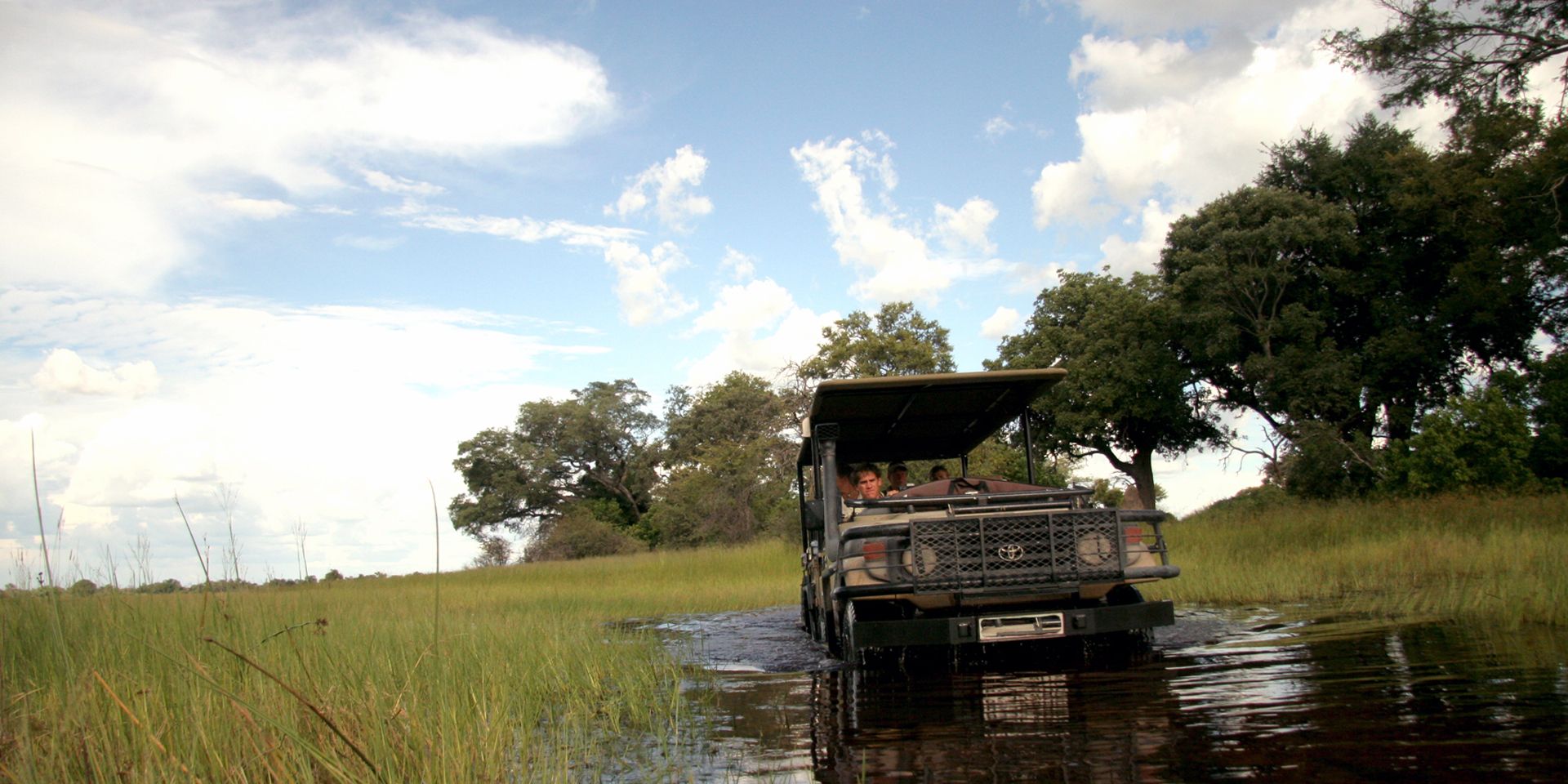 Im Rahmen eines Game drive durch Botswanas Busch durchqueren die Teilnehmer mit einem Gelaendewagen einen Fluss