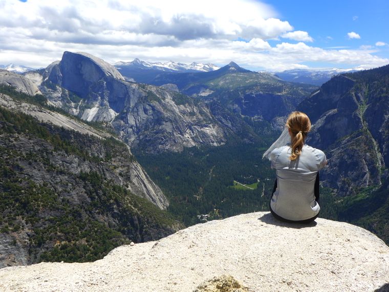 Eine Freiwillige sitzt auf einem Felsvorsprung und blickt auf die Weiten des Yosemite Nationalparks.