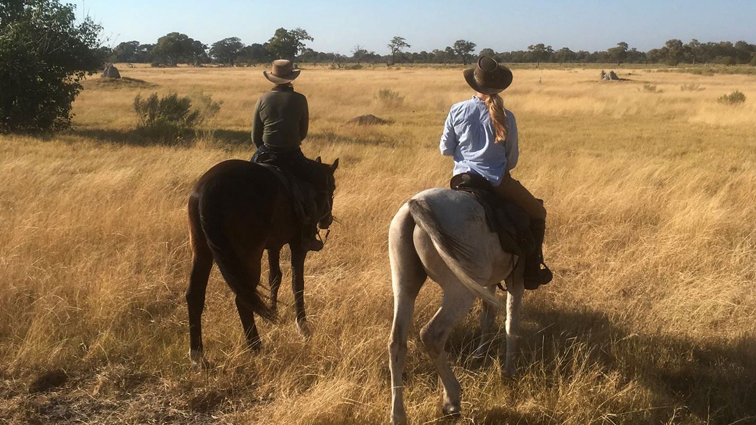 Reittour Afrika: Zwei Safari-Gaeste auf einer Pferdesafari in der afrikanischen Savanne