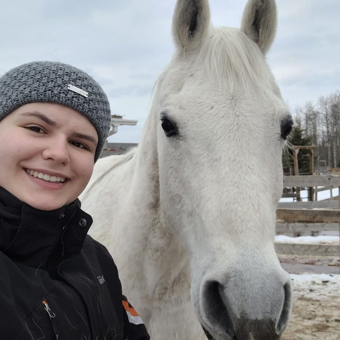 Jessica steht mit einem großen Lächeln im Gesicht neben einem friedlichen Schimmel im Pferdeschutz Projekt als Freiwilligenhelferin in Kanada