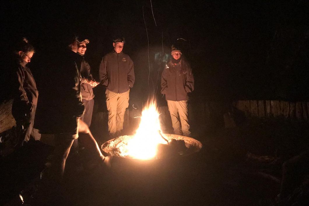 Eine Gruppe von Trails Guide-Studenten steht am abendlichen Lagerfeuer im suedafrikanischen Trainingscamp Ulovane