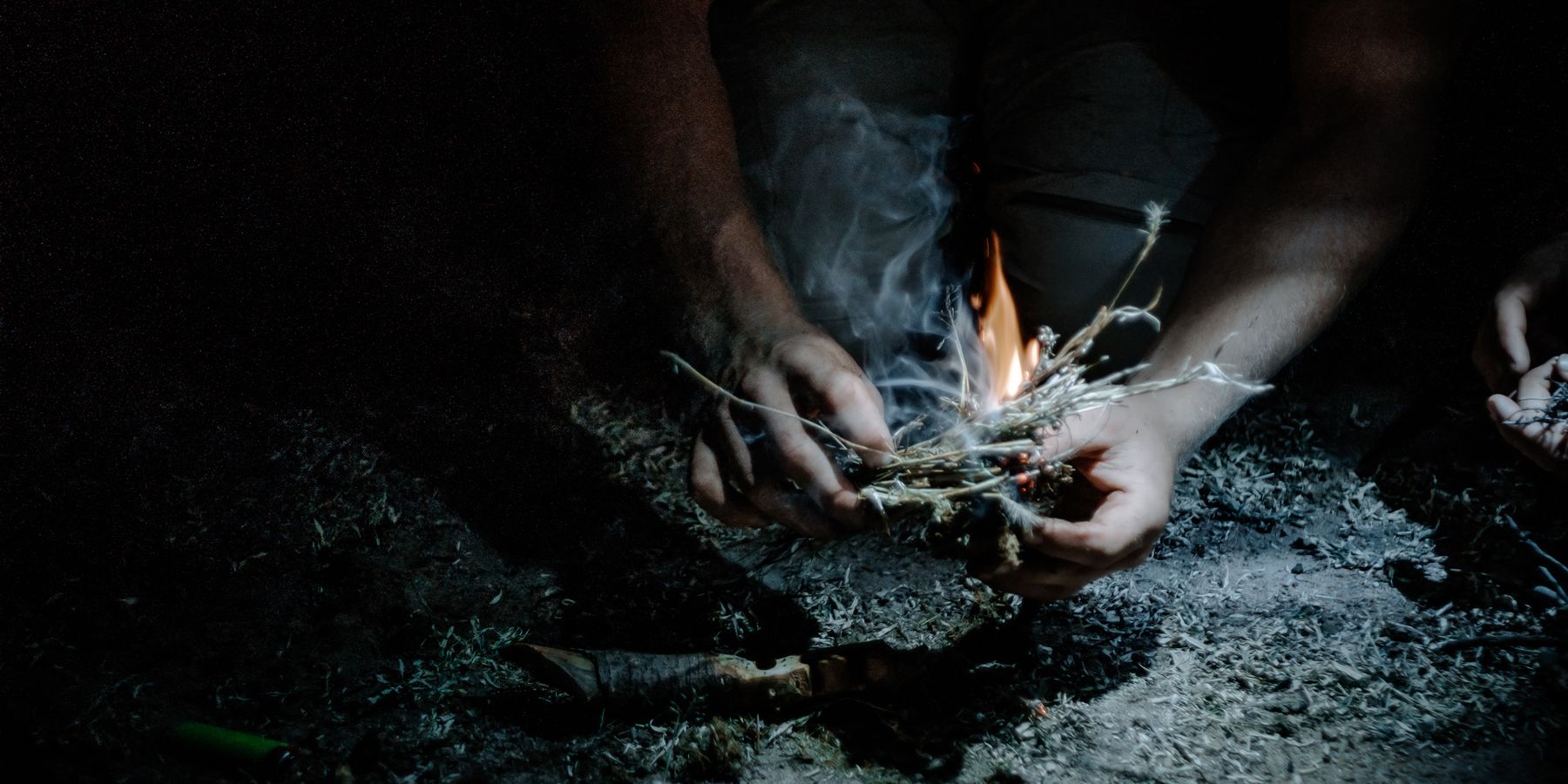 In dieser Nachtaufnahme wirft eine Stirnlampe ein weiß bläuliches Licht auf den Boden. Eine Person hat Feuer entfacht, um ein Lagerfeuer für die Nachtwache des Kalahari Primitive Trail zu machen.