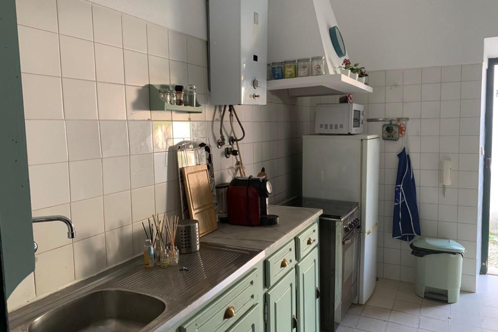 Die gut ausgestattete Küche, in der die Freiwilligen ihre eigenen Lebensmittel zubereiten können, hat hellgrüne Schränke und hohe Decken, sowie eine Tür, die nach Draußen führt.