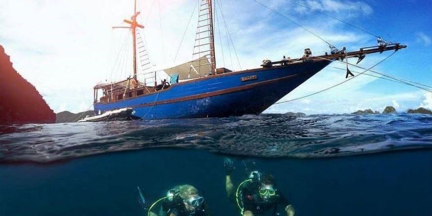 Zwei Personen haben das Tauchsafarischiff (Liveboard) verlassen und begeben sich in die Tiefe der indonesischen Unterwasserwelt auf ihrem Segelurlaub.