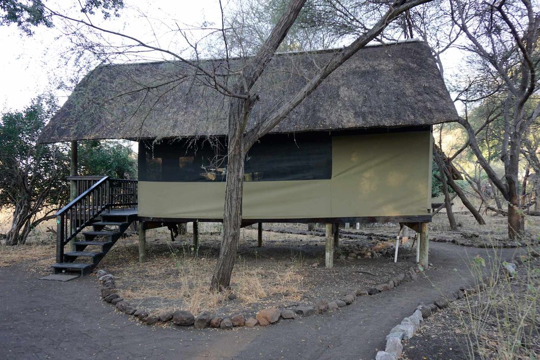 Eine durch Stelzen leicht erhoehte Huette mit Veranda im Camp