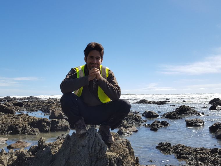 Ein freiwilliger Helfer sitzt auf einem Stein an der Kueste Neuseelands