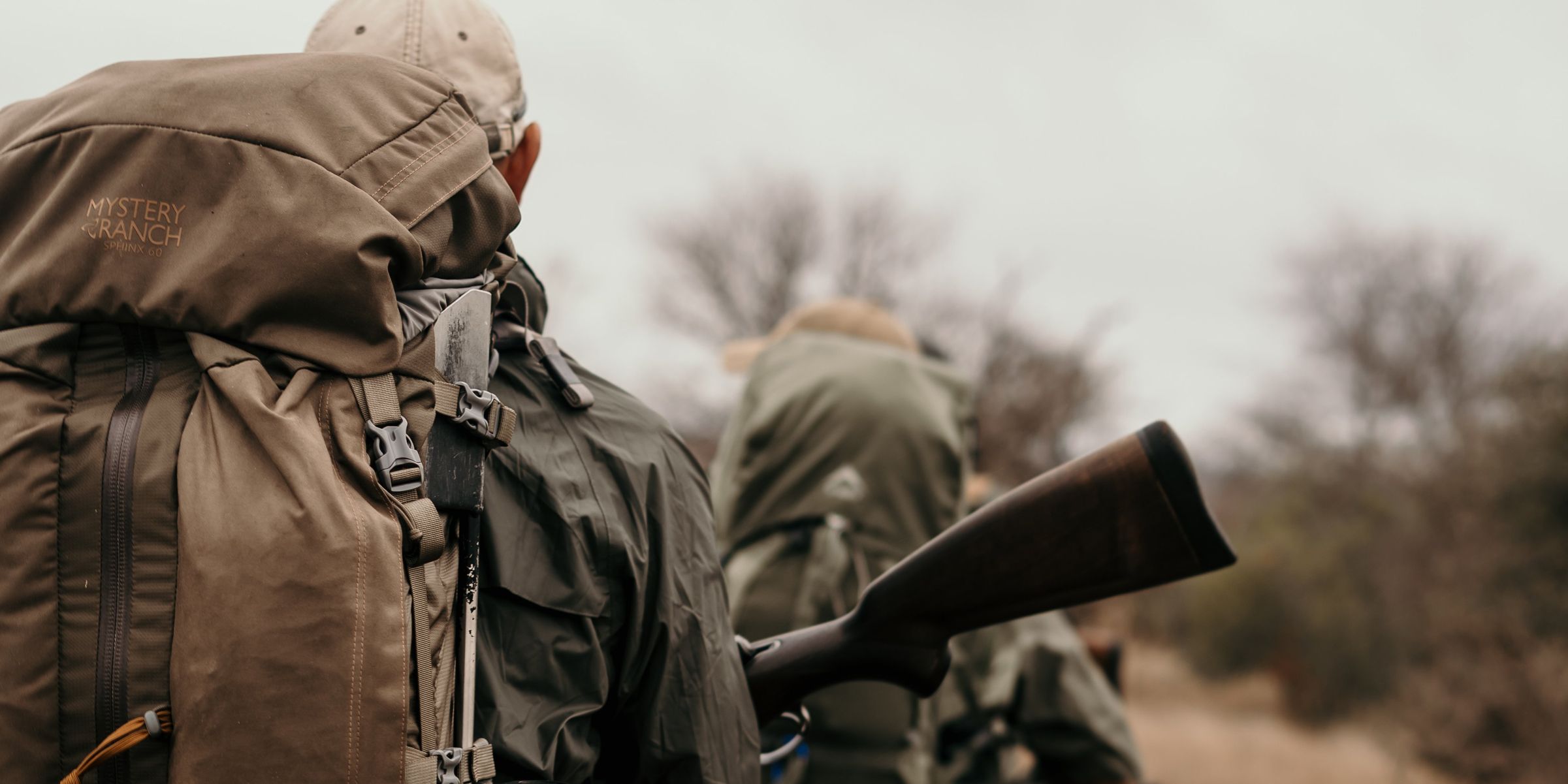 Eine Reisegruppe, bepackt mit Rucksäcken, ist zu Fuß im !Khamab Kalahari Reserve unterwegs.