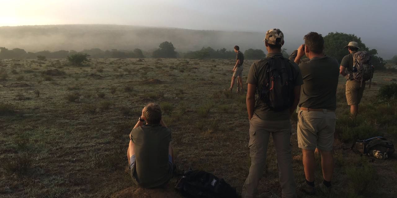 Eine Gruppe von Trails Guide-Studenten steht im suedafrikanischen Amakhala Game Reserve und fokussiert eine noch nicht erkennbare Sichtung