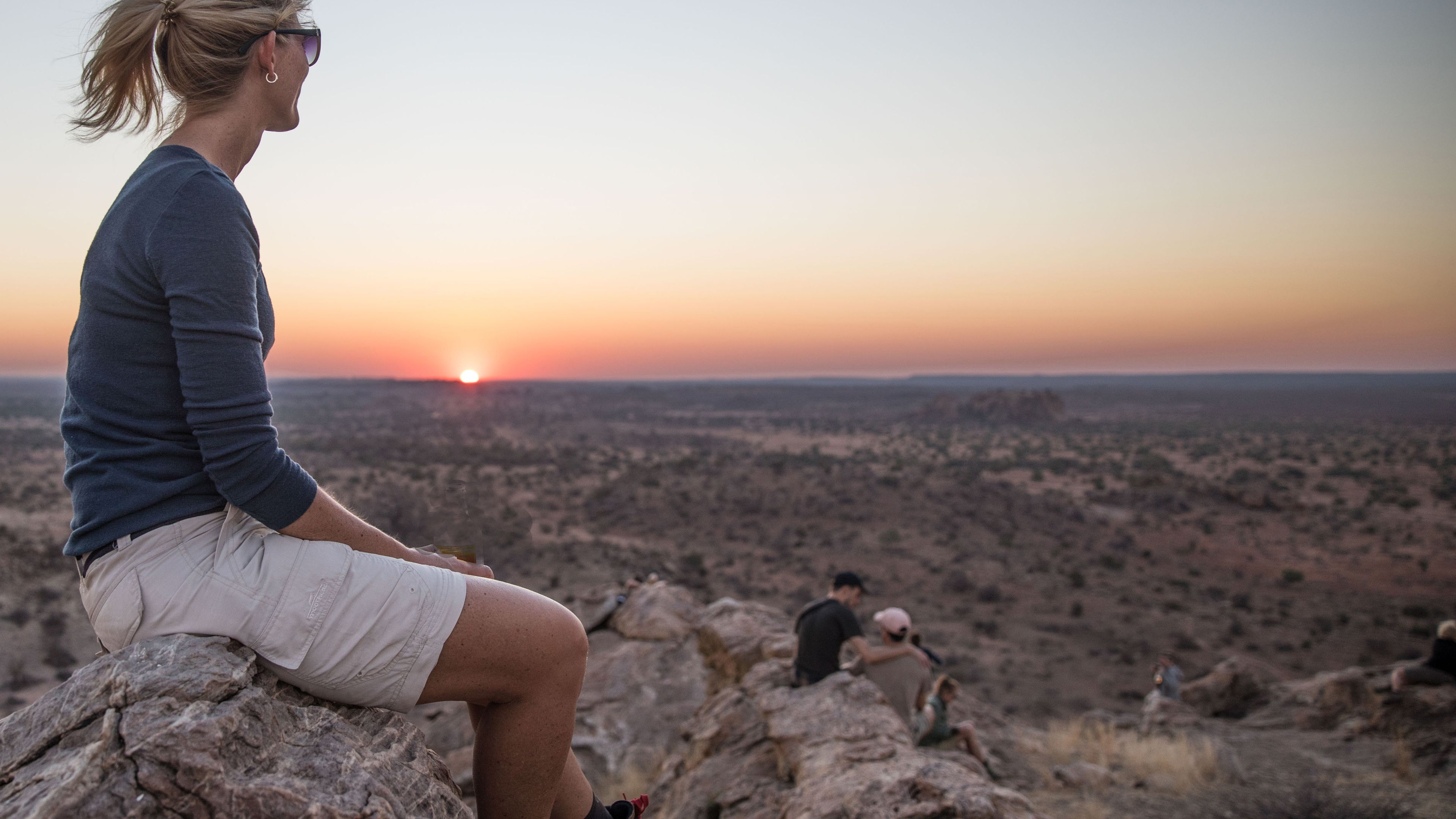 A woman is sitting on a rock watching the sunset
