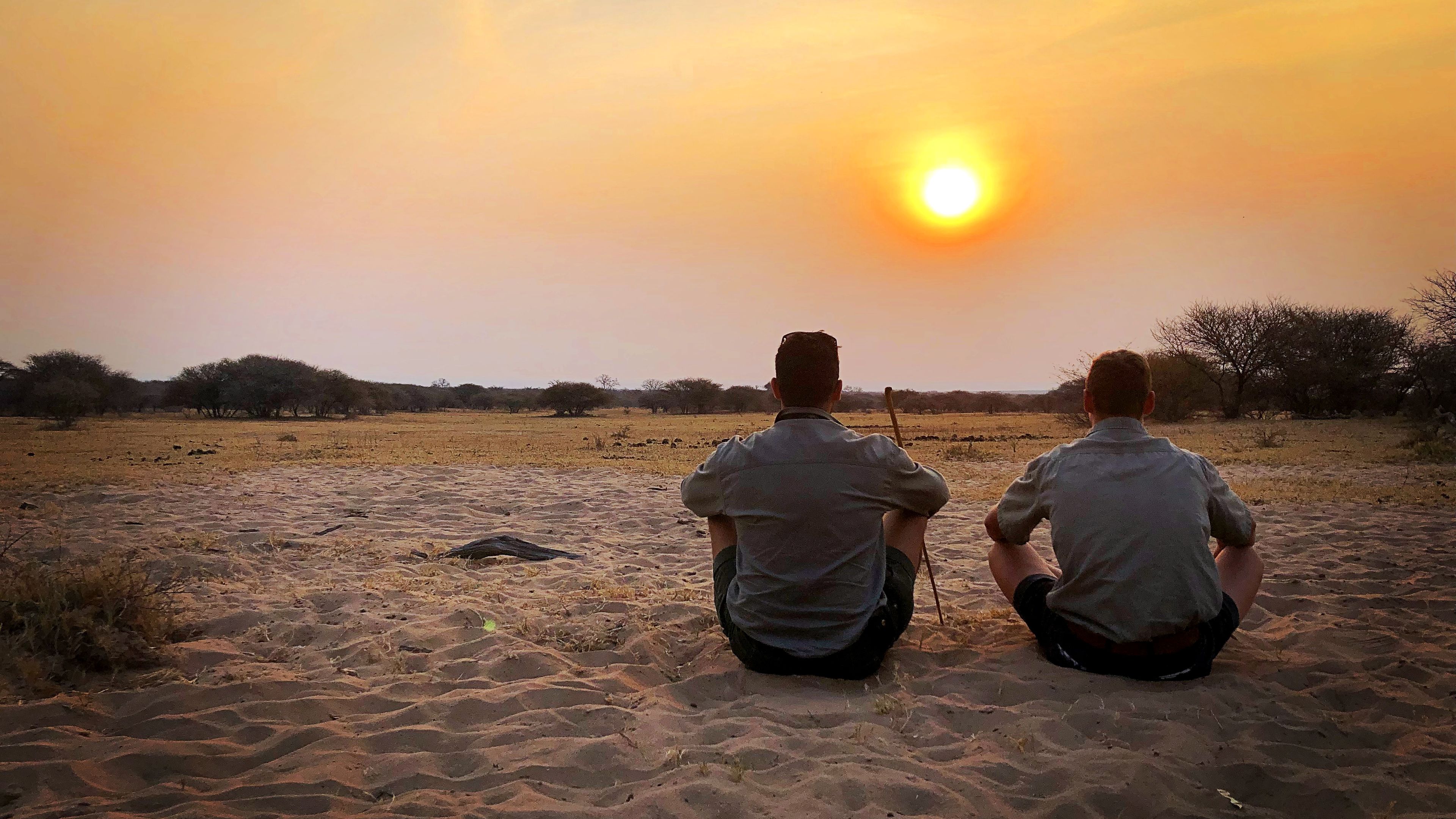 Zwei Field Guide-Studenten sitzen in der Savanne Suedafrikas und beobachten den Sonnenuntergang