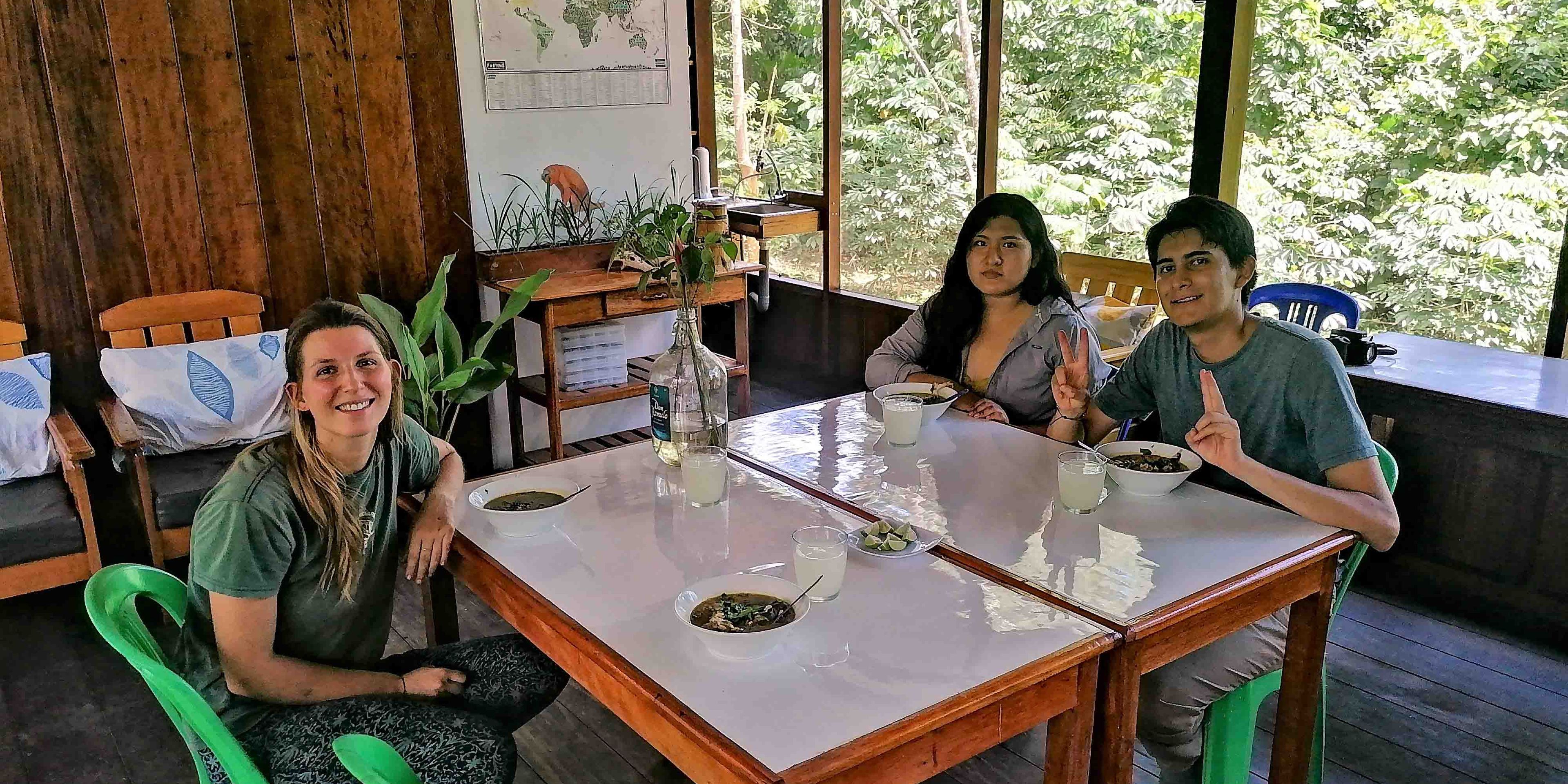 Drei Mitglieder des internationalen Teams der Forschungsstation in Peru sitzen am gemeinsamen Essenstisch und genießen eine Mahlzeit.