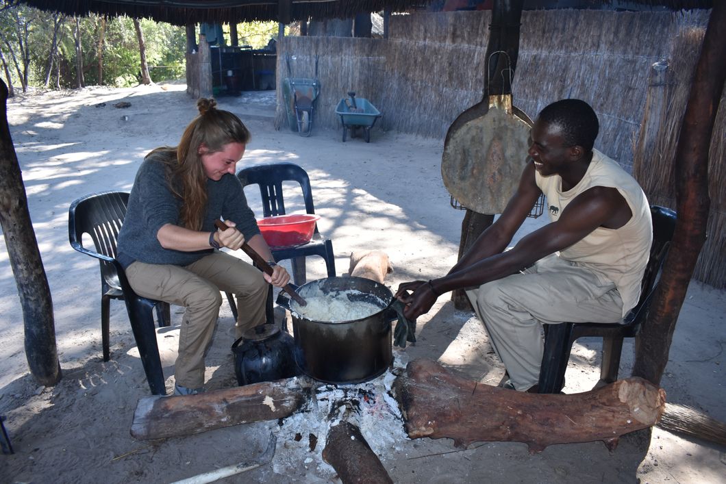 Eine Freiwillige und ein Teamleiter des Elefantenprojekts in Sambia sitzen zusammen im Camp und kochen