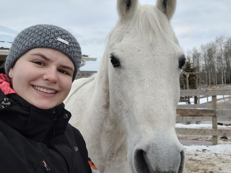 Jessica steht mit einem großen Lächeln im Gesicht neben einem friedlichen Schimmel im Pferdeschutz Projekt als Freiwilligenhelferin in Kanada