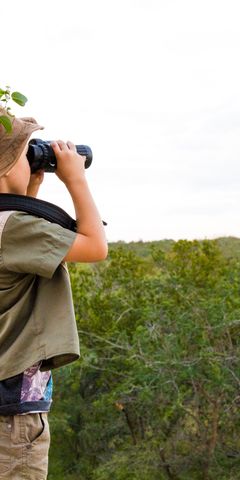 Ein kleiner Junge haelt mit einem Fernglas Ausschau nach Voegeln in der suedafrikanischen Steppe