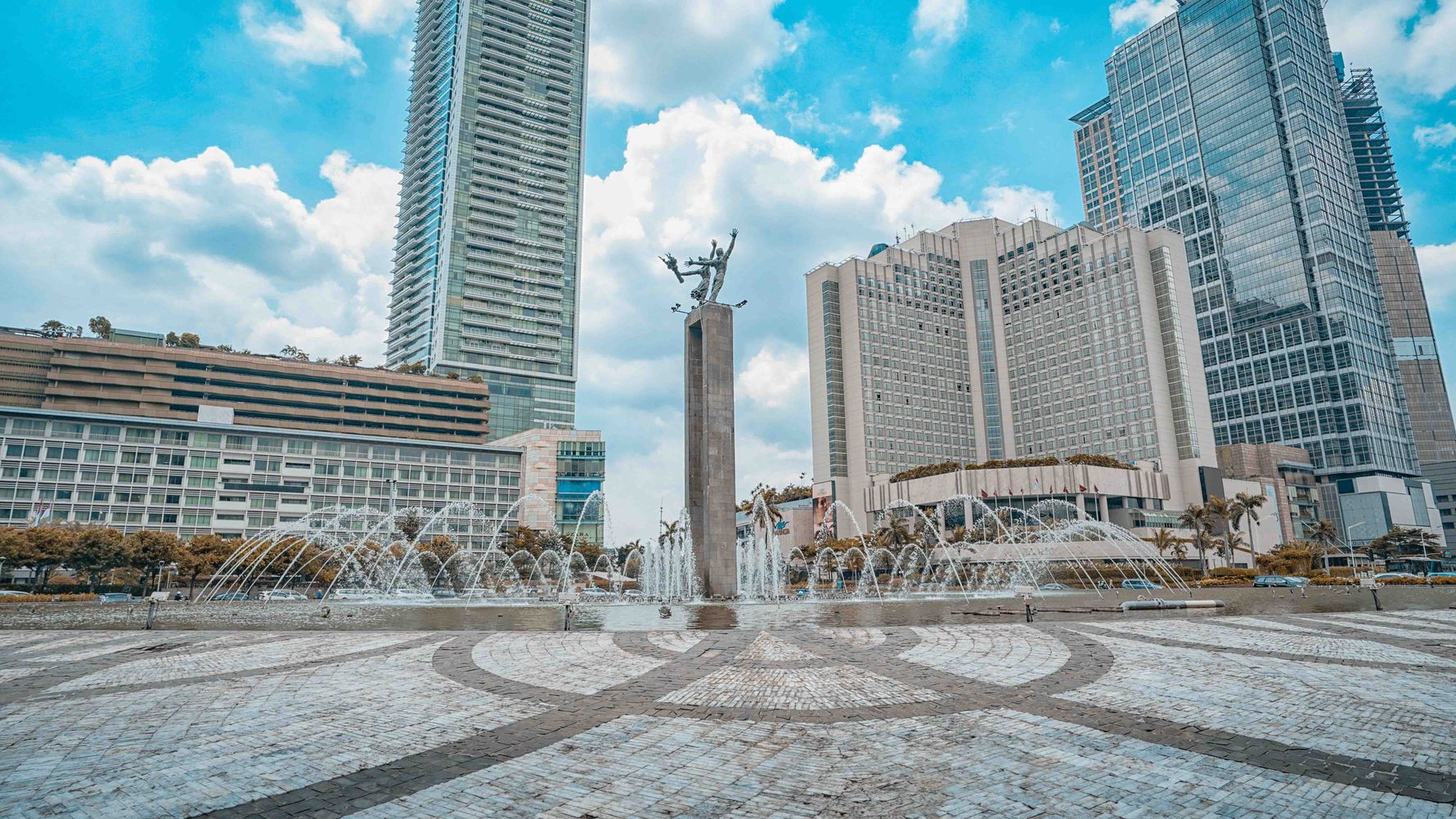 Jakarta, die Indonesiens Hauptstadt, hat eine Willkommensstatur neben einem Springbrunnen mit gläsernen Hochhäusern im Hintergrund.