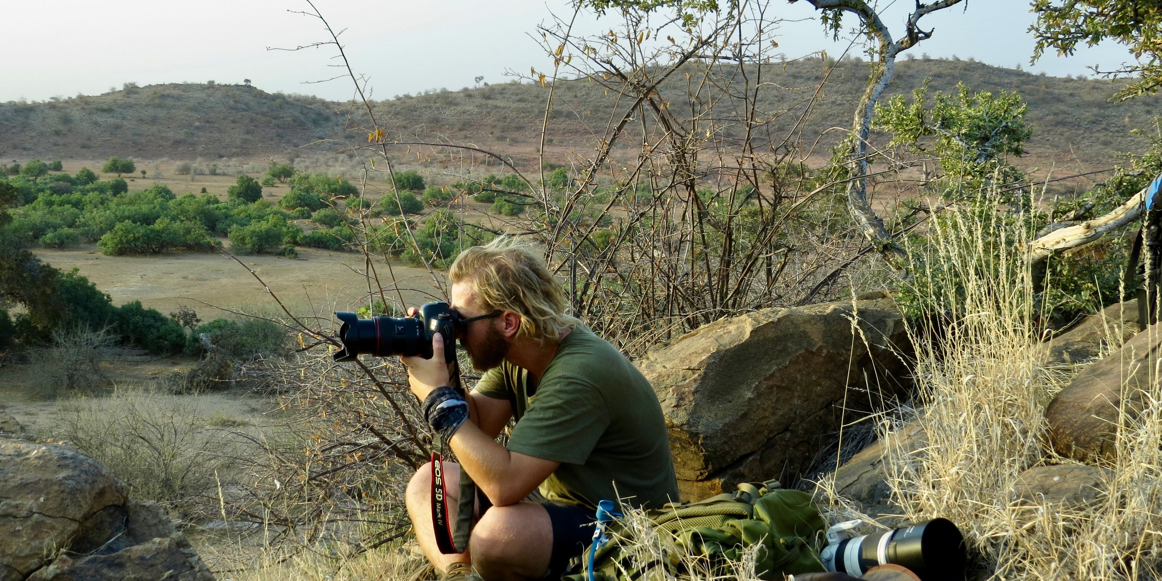 Ein Teilnehmer sitzt im Busch mit seinem Fotoequipment und fotografiert den afrikanischen Busch