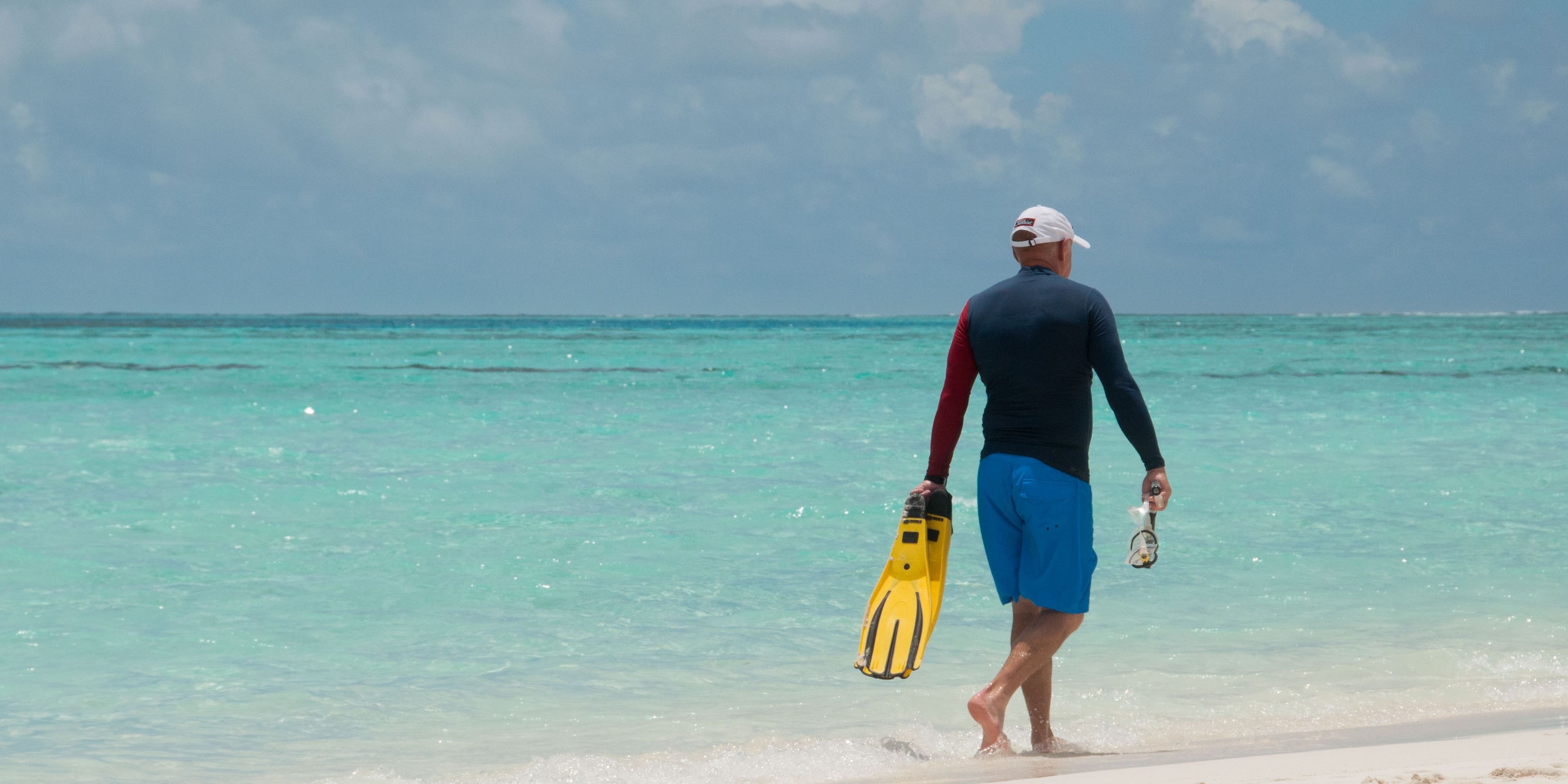 Teilnehmer der Walhai-Expedition auf den Malediven laeuft am Strand entlang, haelt dabei Flossen und Taucherbrille