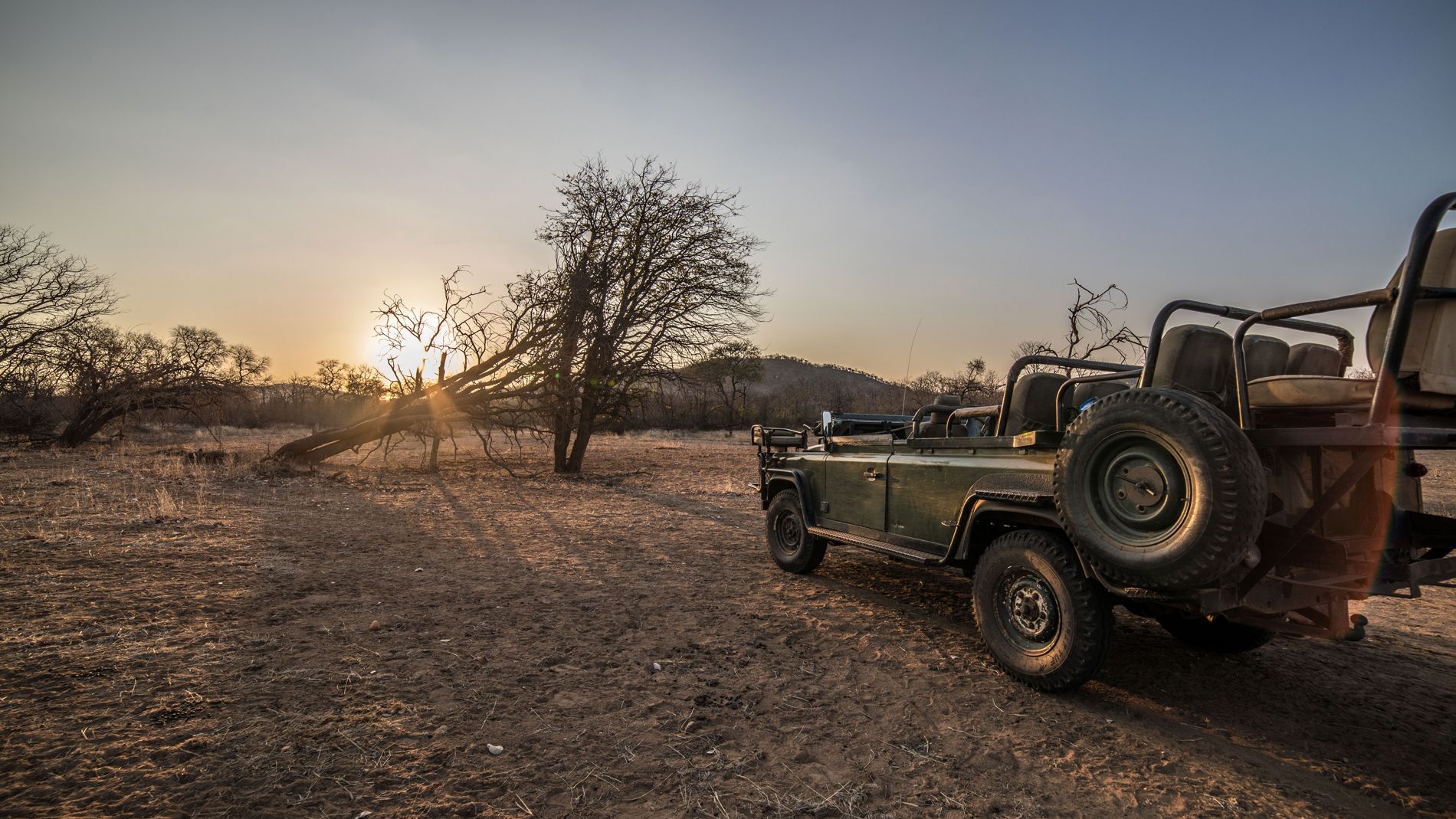 Ein leerer Gelaendewagen steht am Rand der Steppe bei Sonnenuntergang