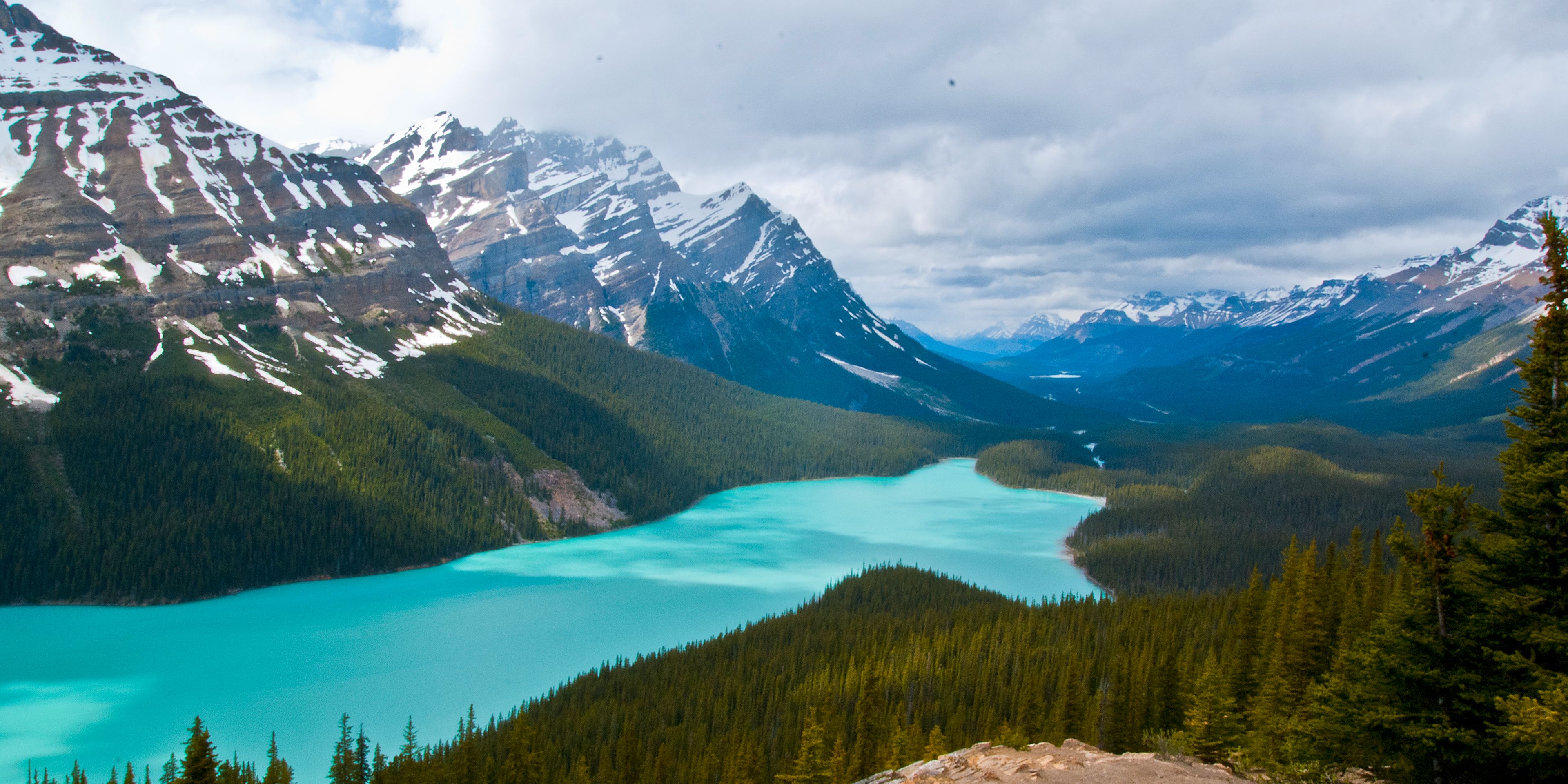 Panoramablick entlang einer verschneiten Gebirgskette mit Vegetationsgrenze und einem grossen See