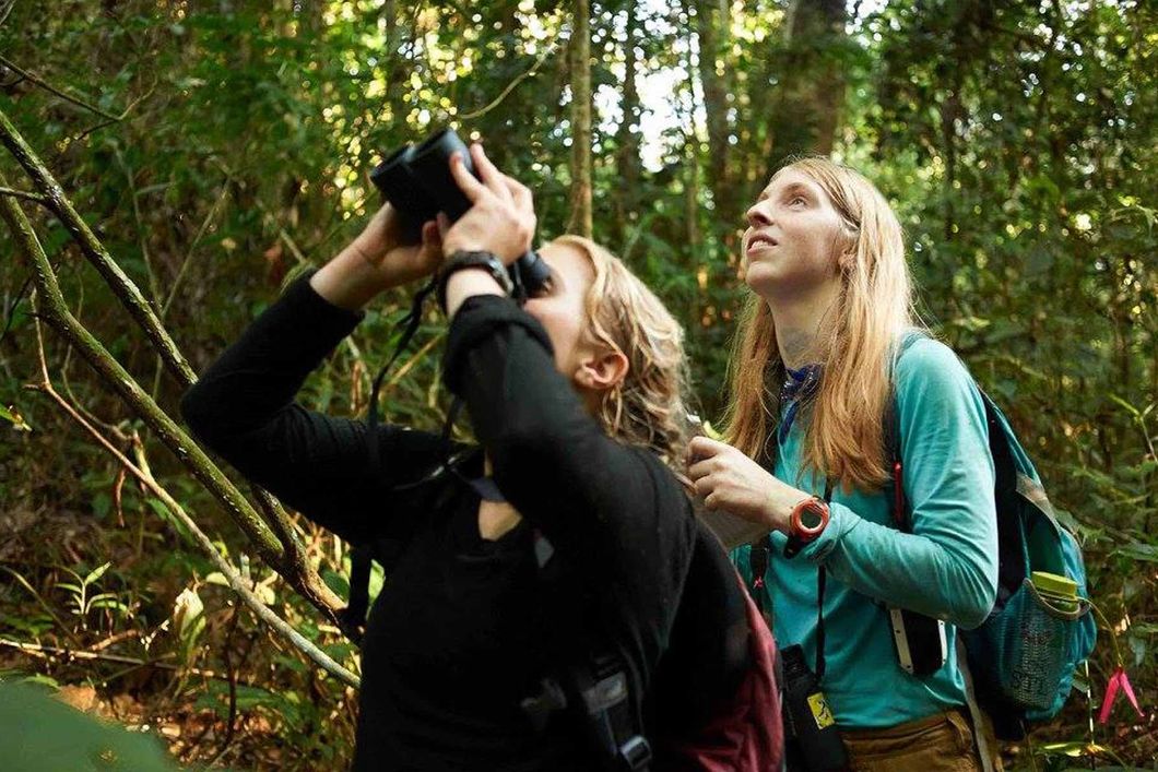 Zwei Praktikantinnen beobachten Voegel mit ihren Fernglaesern und notieren wichtige Daten