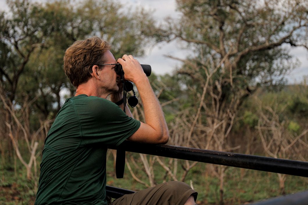 A volunteer participant in South Africa uses binoculars to observe animals.