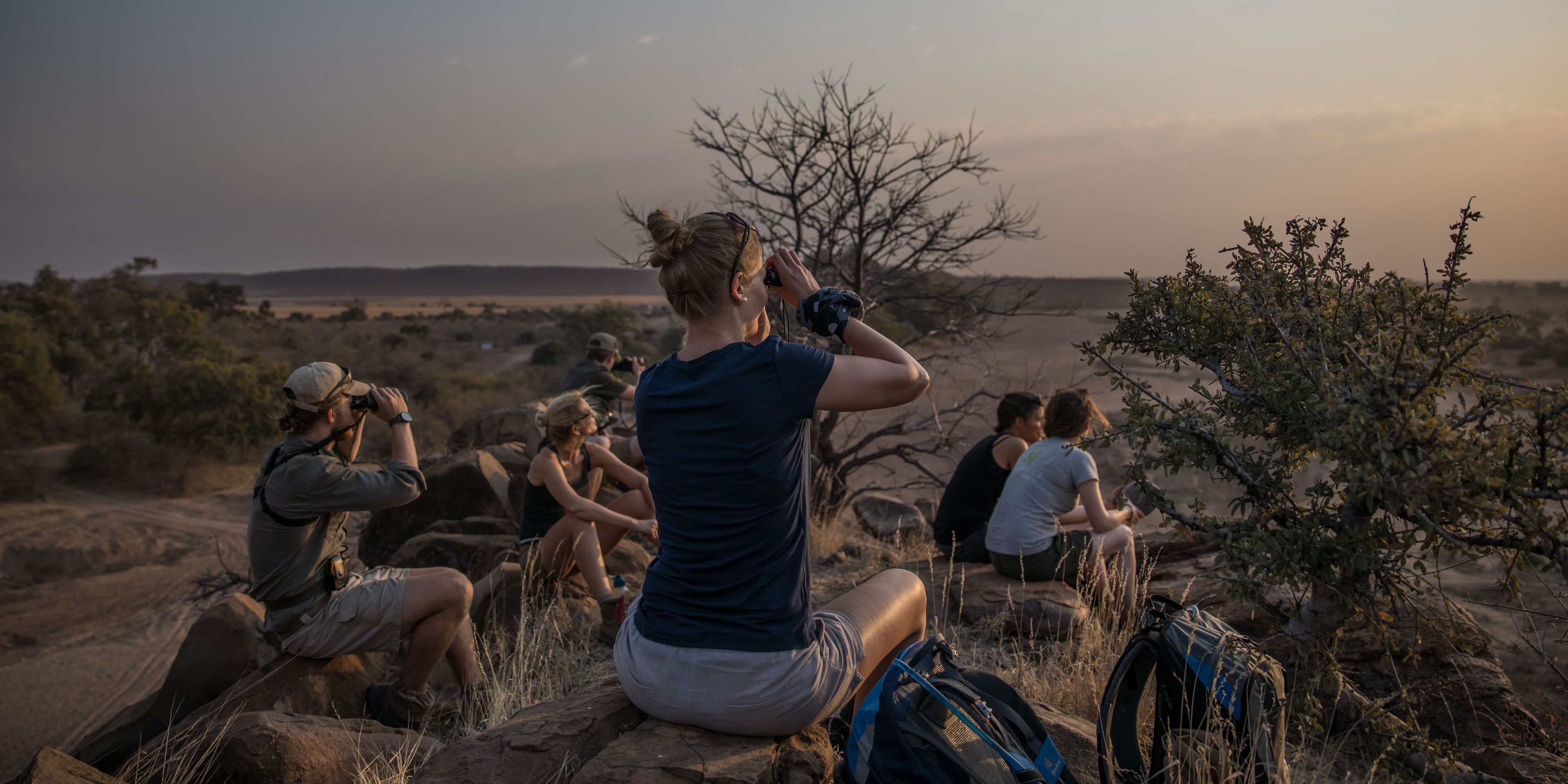 Eine Gruppe von Teilnehmern sitzt auf einem erhoehten Felsenberg, um so per Fernglas Ausschau halten zu koennen