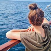 Elisabeth sitzt auf dem Boot, welches ihr in den Malediven für zwei Wochen als Unterkunft dient, und lehnt sich über die Reling. Wir sehen sie von hinten und genießen somit dieselbe Aussicht auf das tief blaue Meer.