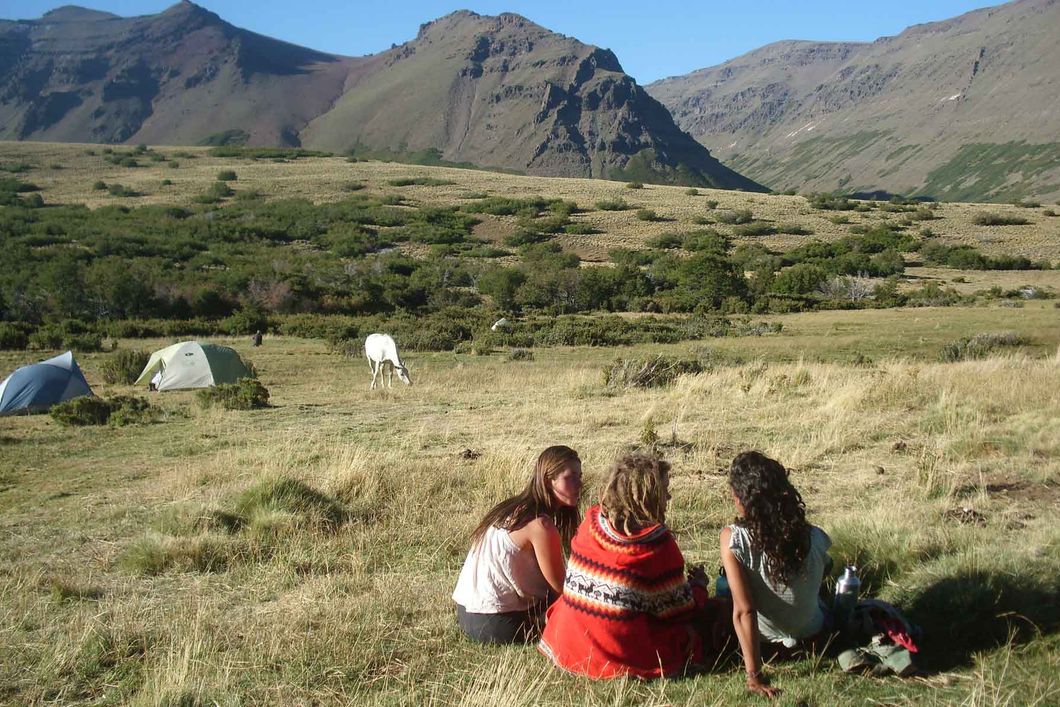 Drei Praktikanten sitzen auf einer Grasebene und geniessen die Aussicht auf die argentinischen Anden