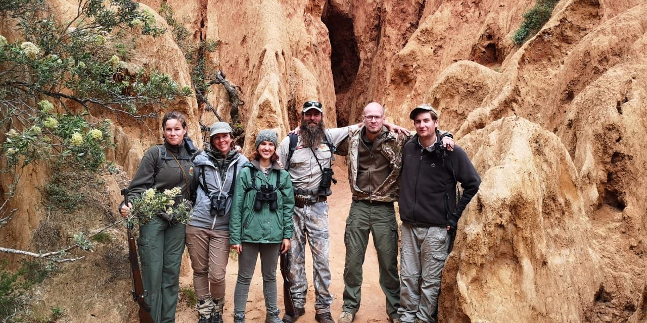 Aufnahme einer Gruppe von Trails Guide-Studenten, die im suedafrikanischen Amakhala Game Reserve vor einem Felsgebilde steht