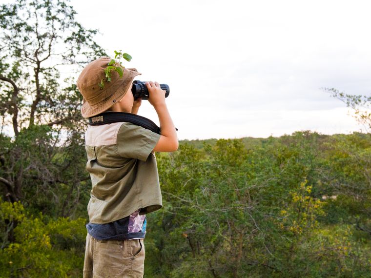 Ein kleiner Junge haelt mit einem Fernglas Ausschau nach Voegeln in der suedafrikanischen Steppe
