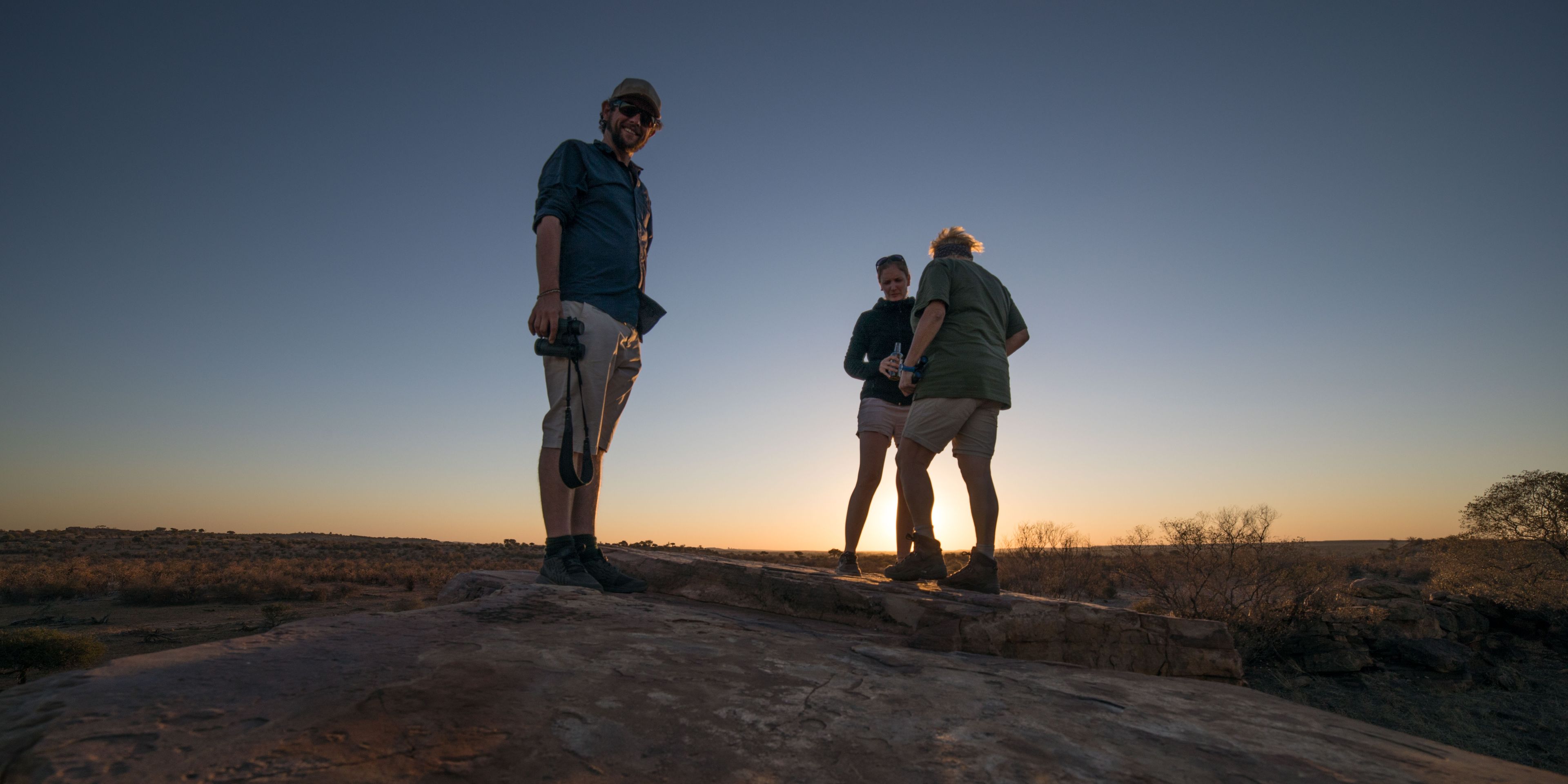 Drei Teilnehmer stehen auf einem Felsen in der Steppe bei Sonnenuntergang