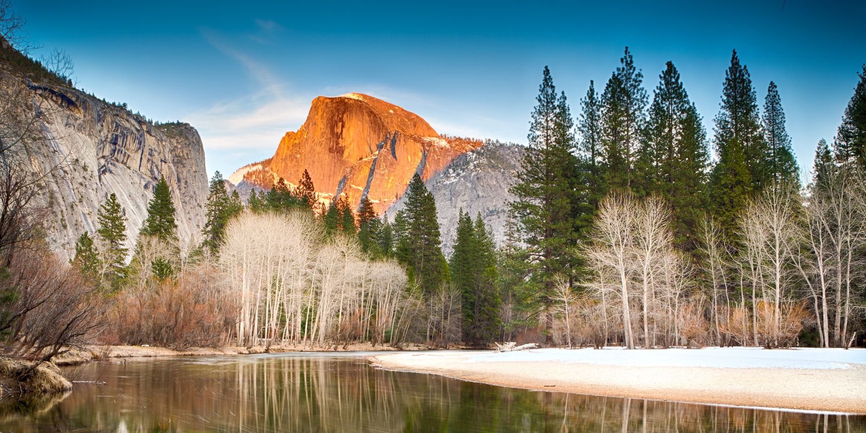 Ein stiller, klarer See bietet eine nahezu makellose Reflexion eines Waldes und eines Berges im Hintergrund