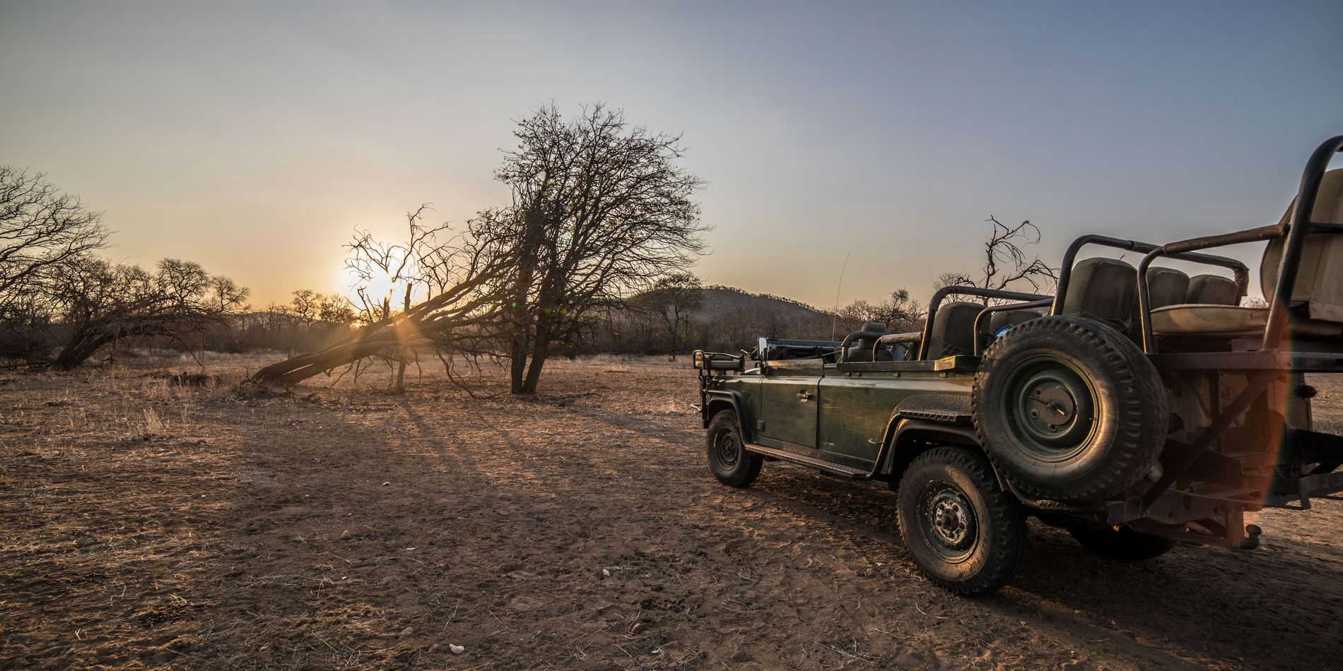 Ein leerer Gelaendewagen steht am Rand der Steppe bei Sonnenuntergang