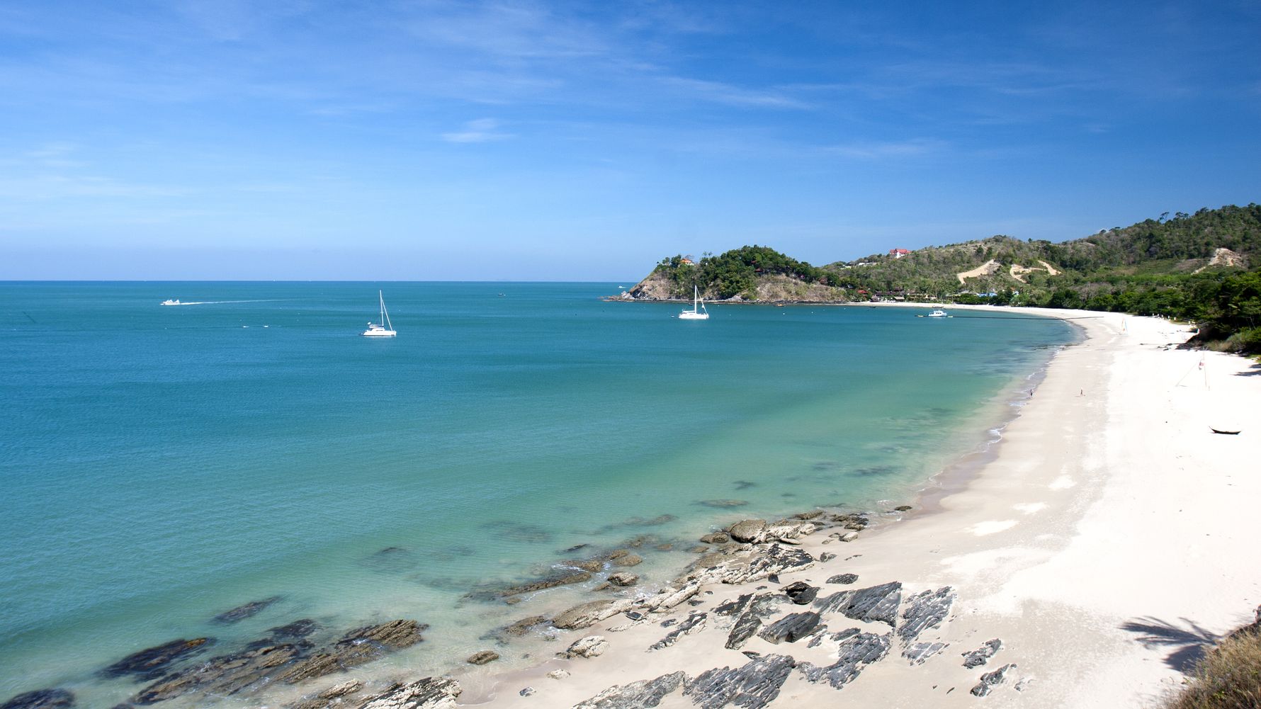 Ein thailaendischer Kuestenabschnitt mit turekisblauem Wasser und einigen Booten im Ozean