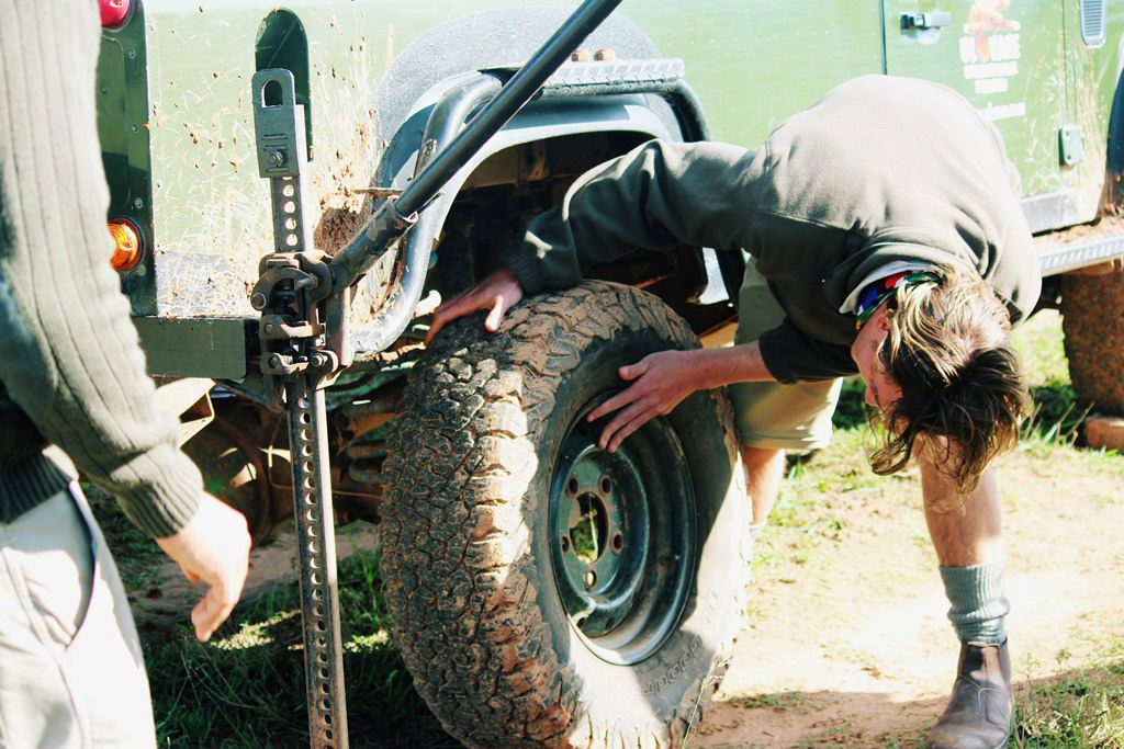 Ein Field Guide-Student nimmt einen Reifenwechsel an einem offenen Gelaendewagen in Suedafrika vor
