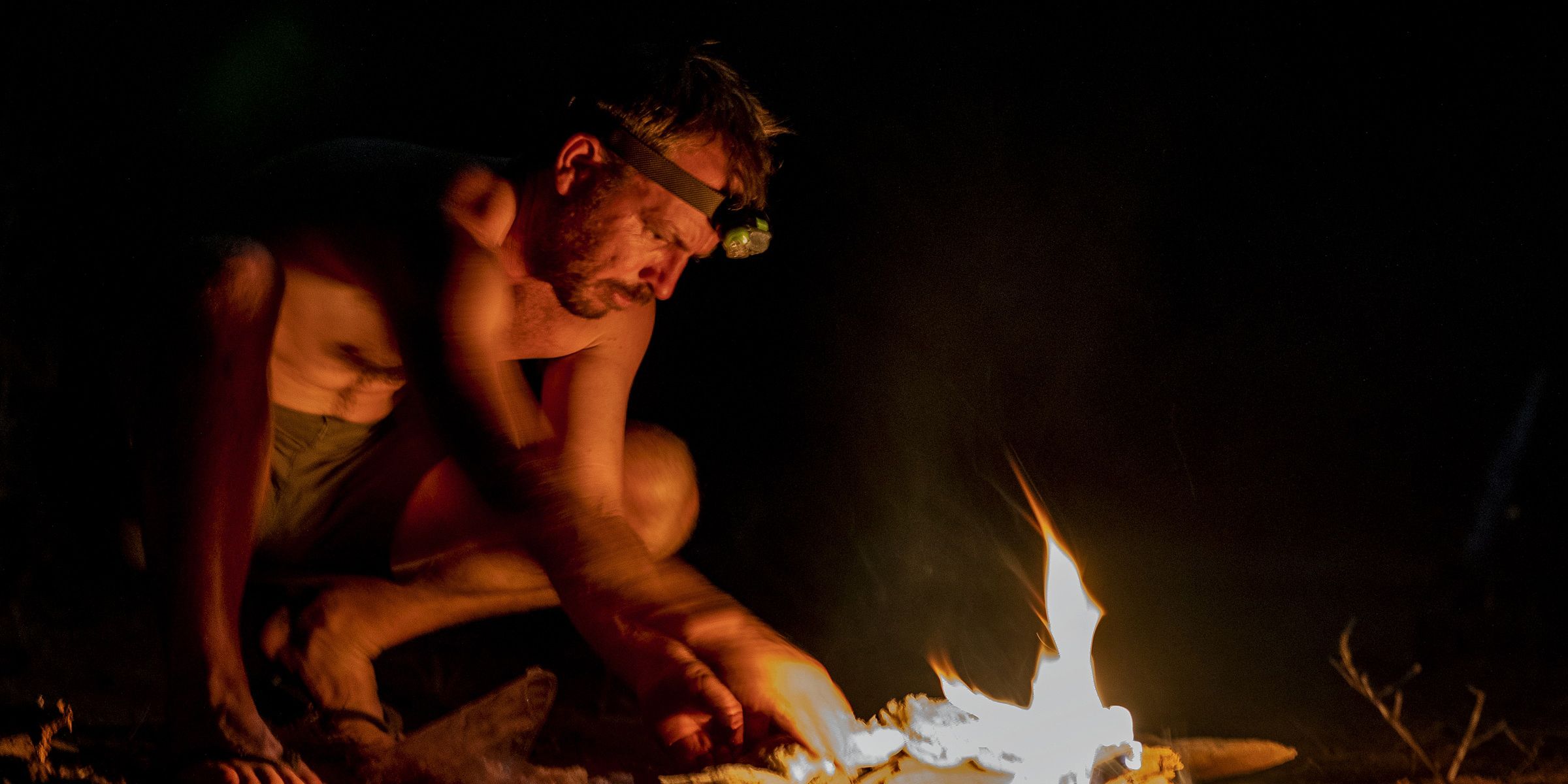 In the dark nights, a flickering campfire lights up the night camp on the Primitive Trail. The course leader has crouched down next to the fire and makes sure it keeps burning.