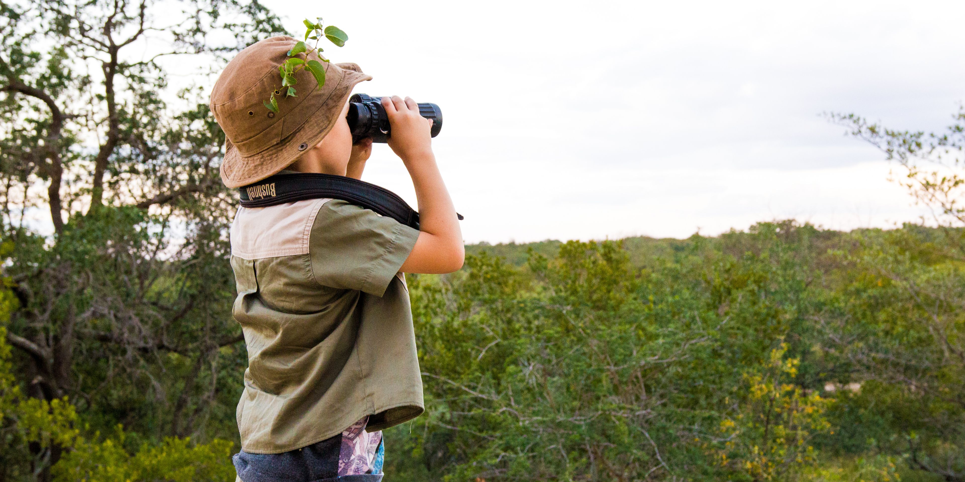 Ein kleiner Junge haelt mit einem Fernglas Ausschau nach Voegeln in der suedafrikanischen Steppe