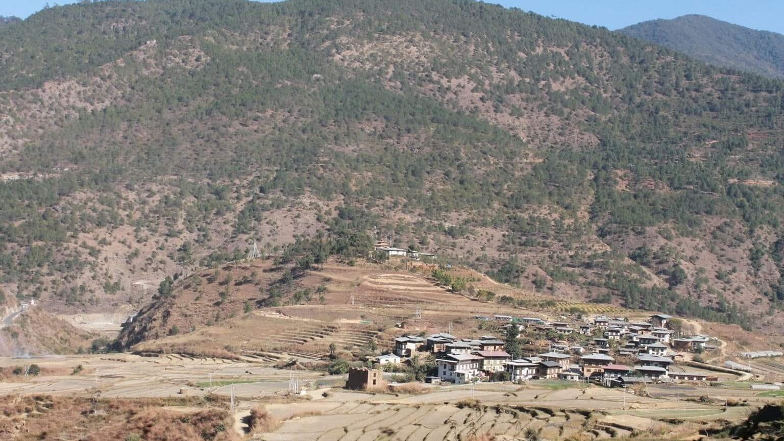 Blick ueber eine kleine Siedlung, angegliederte Plantagen und Waldlandschaft in Bhutan.