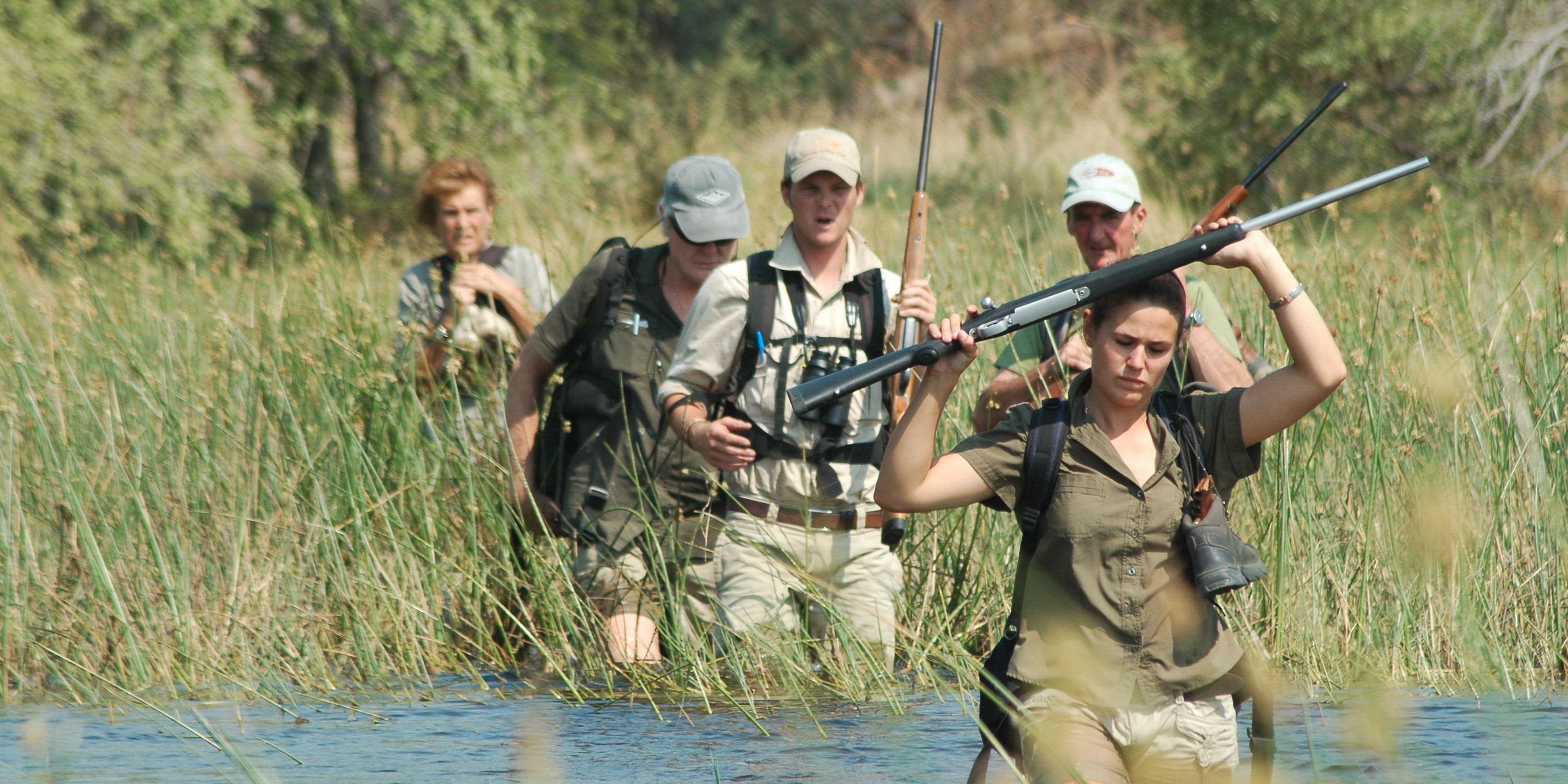 Teilnehmer des Natur- und Rangerkurses waten durch ein flaches Gewaesser waehrend einer Pirschwanderung