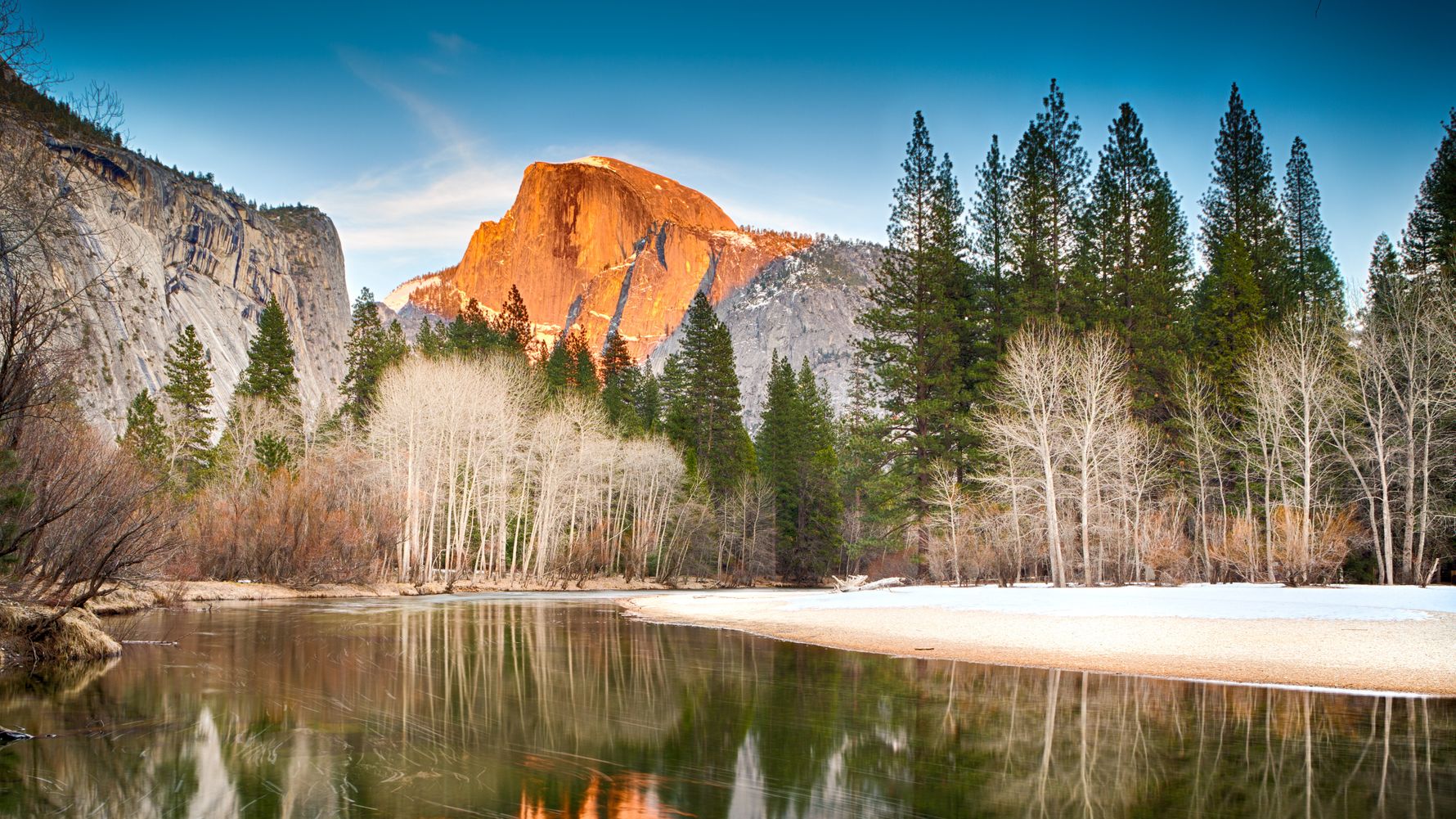 Ein stiller, klarer See bietet eine nahezu makellose Reflexion eines Waldes und eines Berges im Hintergrund