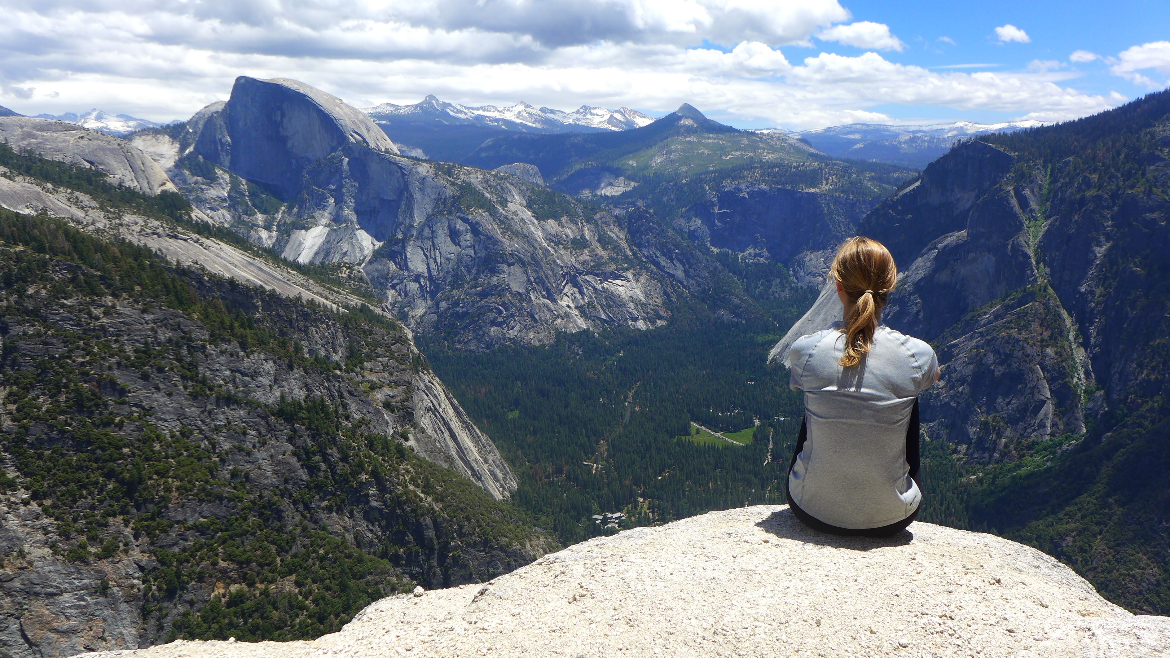 Eine Freiwillige sitzt auf einem Felsvorsprung und blickt auf die Weiten des Yosemite Nationalparks.