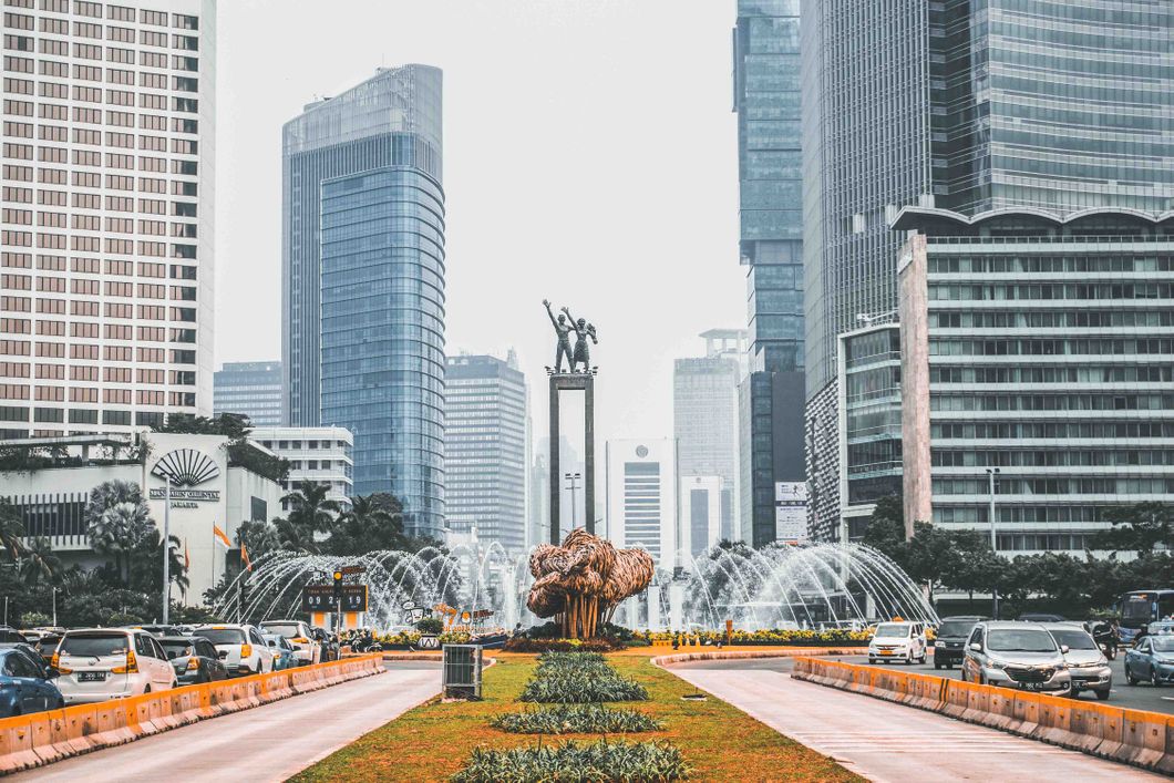 Die Willkommensstatur in Jakarta, der Hauptstadt Indonesiens, steht vor einem Springbrunnen umgeben von befahrenen Straßen mit gläsernen Hochhäusern im Hintergrund.