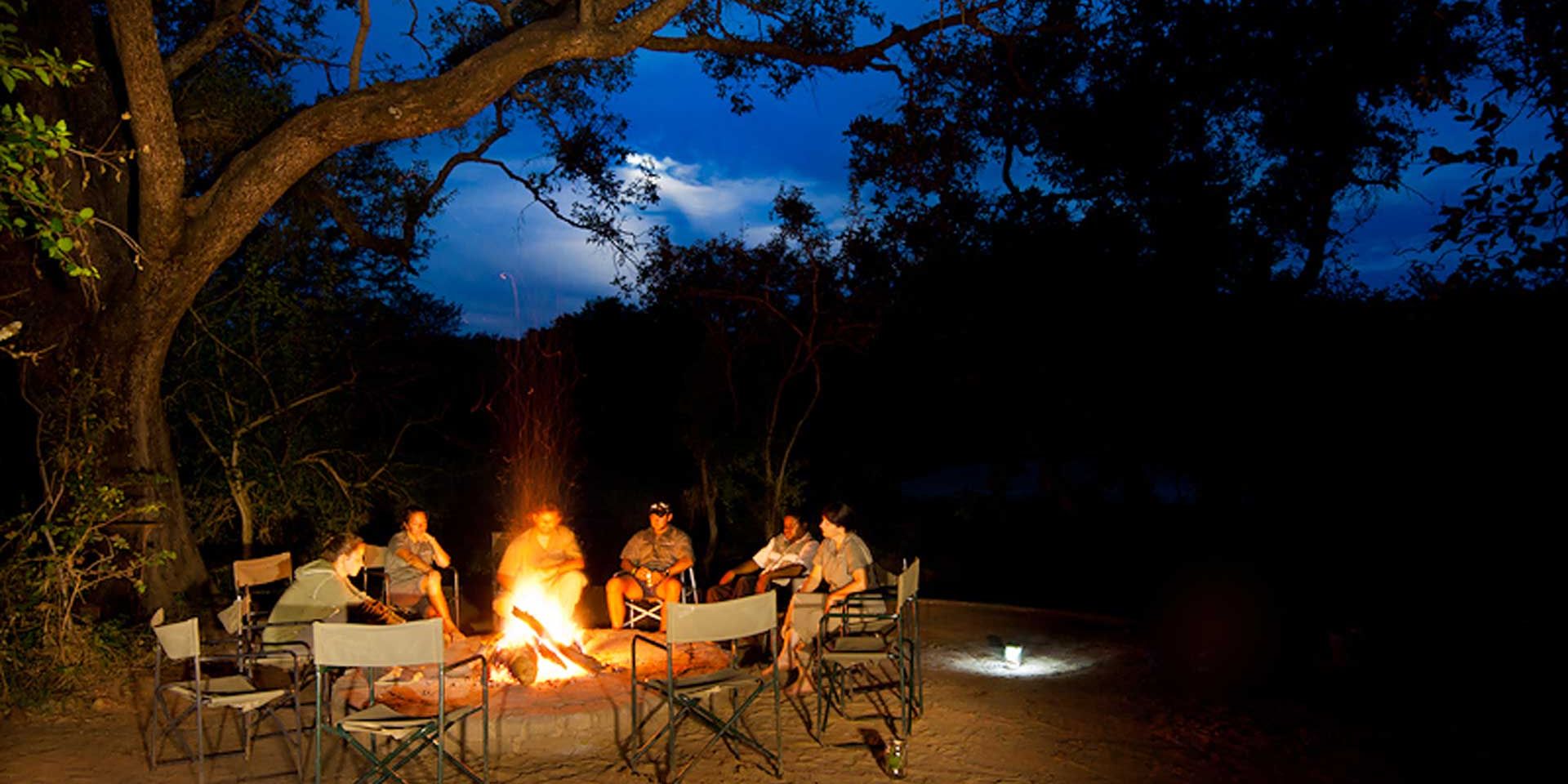 Eine Gruppe von Teilnehmern einer Erlebnisreise durch Suedafrika sitzen in gemuetlicher Runde am Lagerfeuer
