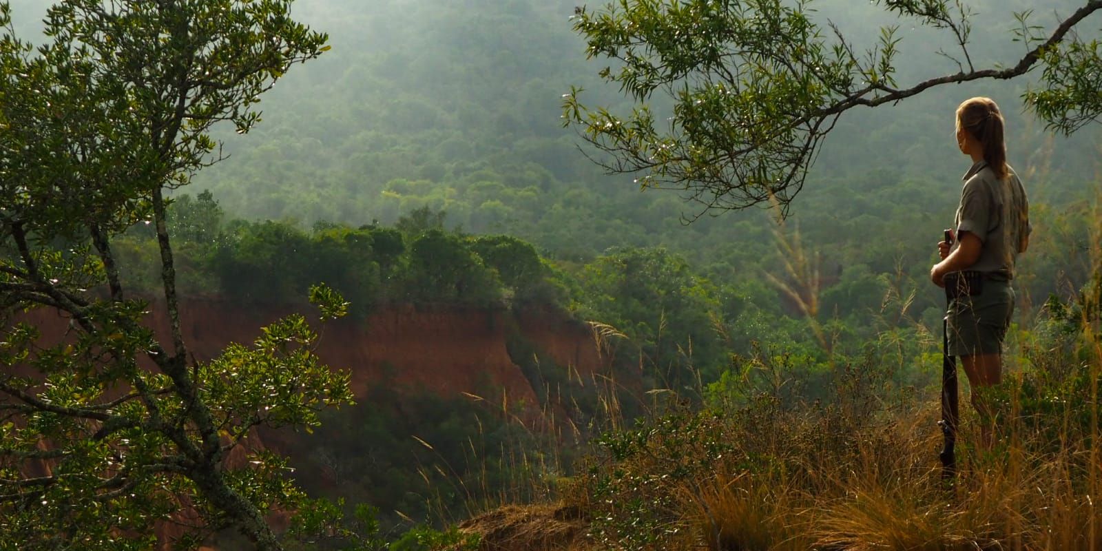 Eine Trails Guide-Studentin steht inmitten der wilden Natur des Amakhala Game Reserves und laesst den Blick ueber die weite Landschaft schweifen